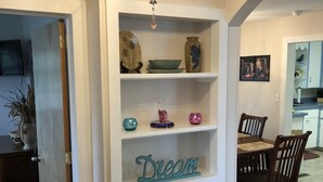 Un comedor con una mesa y sillas de madera, una pared blanca con estantes que exhiben objetos decorativos y una lámpara de araña.