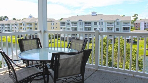 A covered outdoor area with a glass table and four chairs, overlooking a residential complex with multiple buildings. - Just an 8 Minute Drive to the Beach.... (Myrtle Beach)
