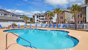 A swimming pool with blue chairs and a lifeguard sign, surrounded by brick buildings and palm trees. - Just an 8 Minute Drive to the Beach.... (Myrtle Beach)
