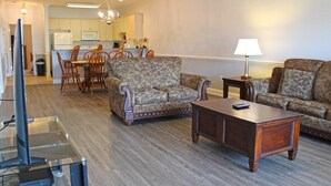 A living room with a sofa, a coffee table, and a TV on a stand. There is a dining area with chairs and a table in the background. - Just an 8 Minute Drive to the Beach.... (Myrtle Beach)