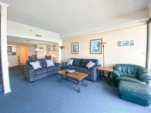 A living room with two grey sofas, a coffee table, a green leather armchair, and a small table with a lamp. - Direct Ocean Front Penthouse! Indoor/outdoor Pool! (Myrtle Beach)