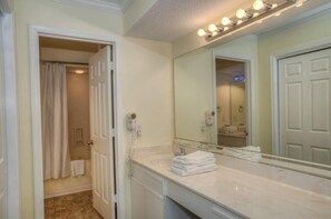 A bathroom with a large mirror, a vanity with a sink, and a shower area.