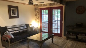 Uma sala de estar com sofá escuro, mesa de centro de vidro, parede de pedra, porta vermelha e ventilador de teto.