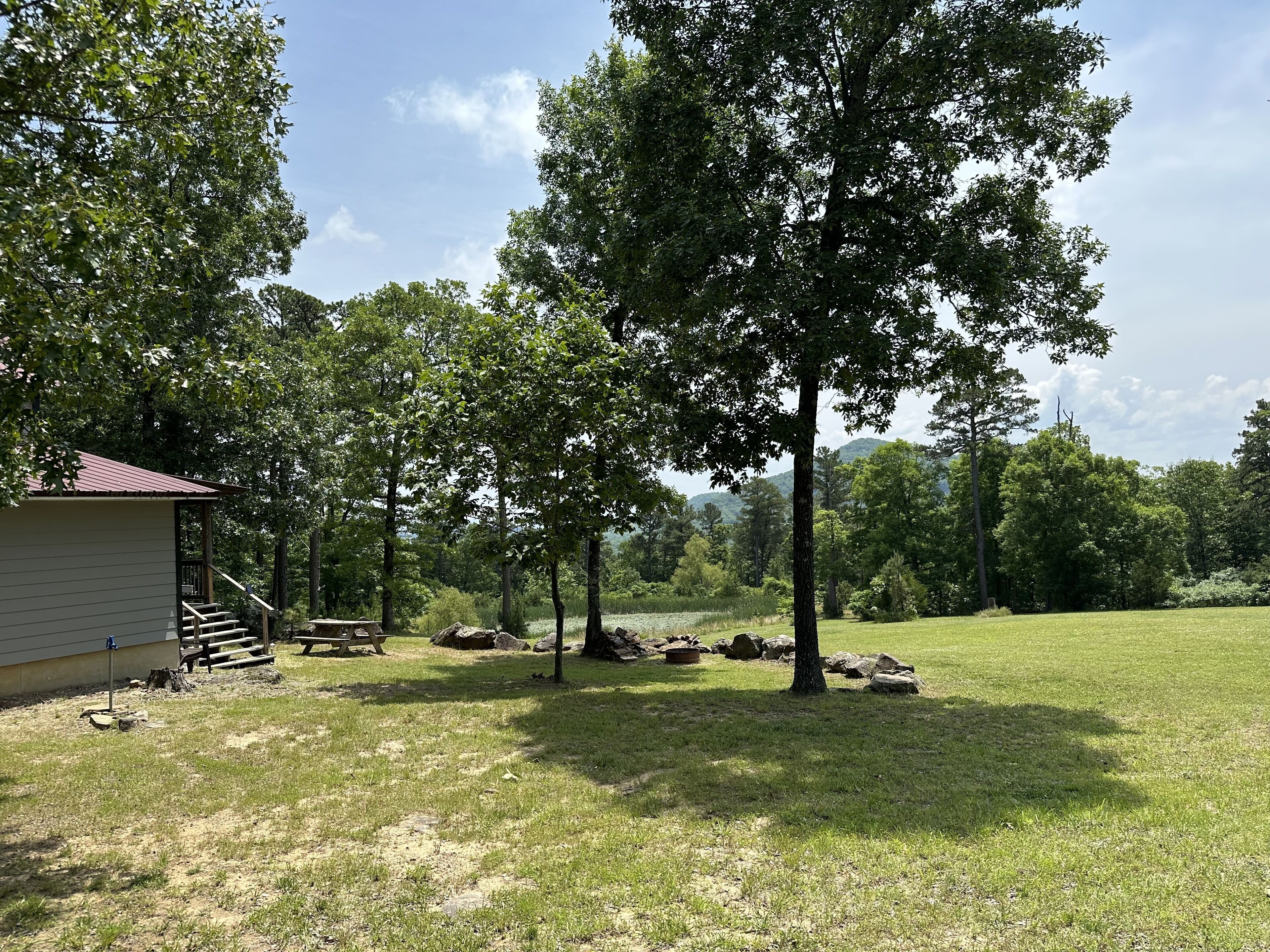 A rustic cabin with a small porch and steps, surrounded by a grassy field and trees.
