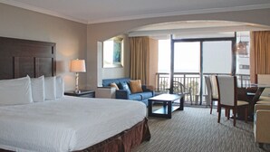 A hotel room with a large bed, a sofa, a dining table, and a balcony with chairs. - Oceanview Villa With NEW Furniture! (Myrtle Beach)