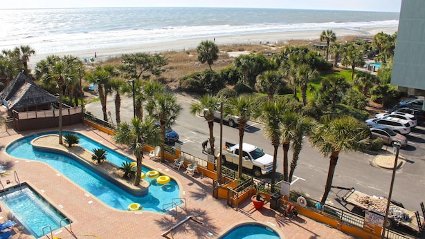 A resort with a swimming pool, palm trees, and a beach view. - Oceanview Villa With NEW Furniture! (Myrtle Beach)