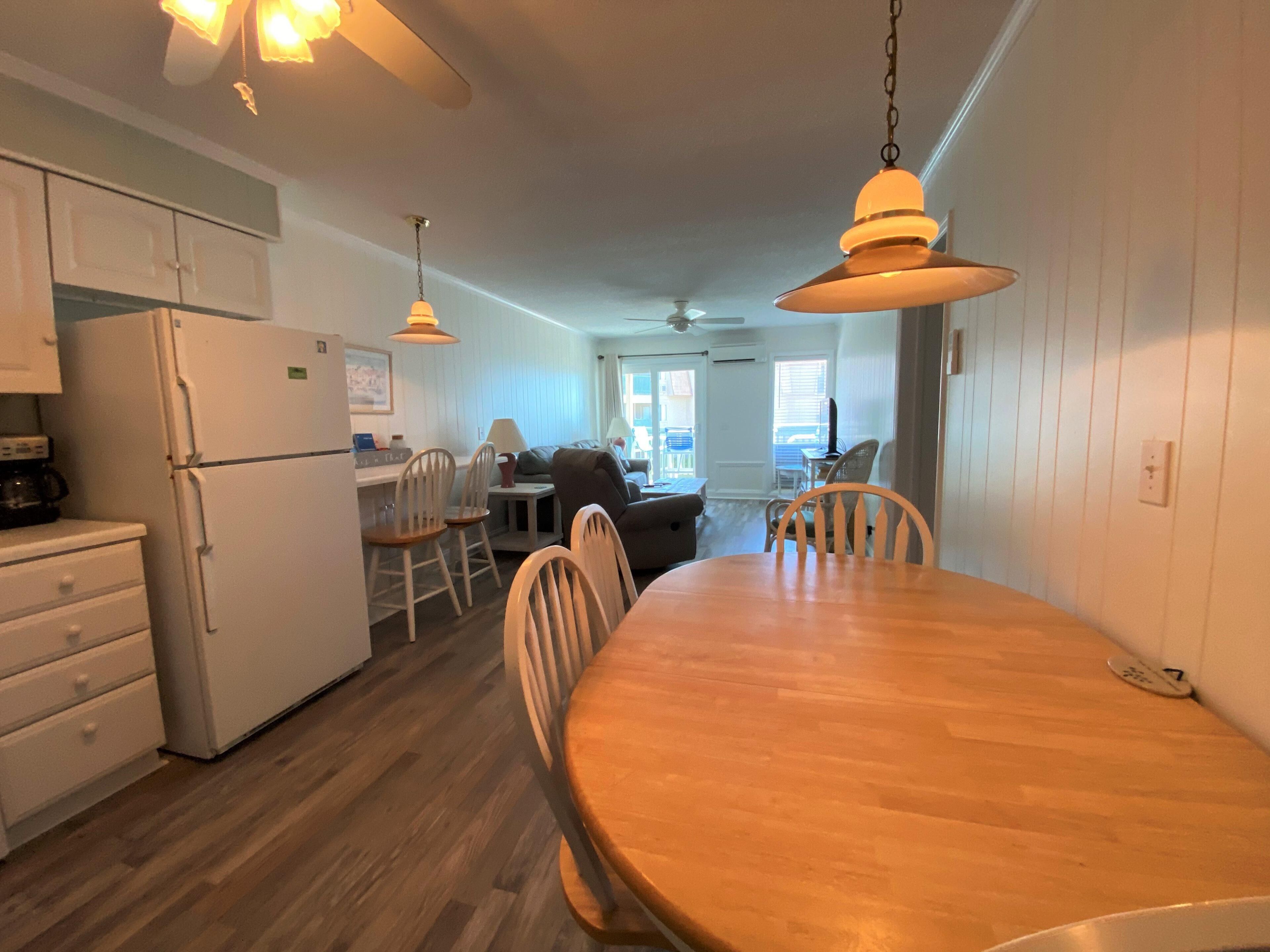 A compact kitchen with white cabinets, a wooden dining table, and a ceiling fan.