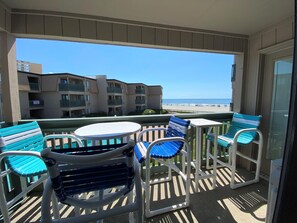 Un balcon avec une table et des chaises, donnant sur une plage et des immeubles.