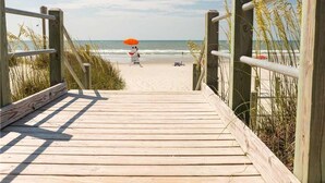 Une promenade en bois menant à une plage où se trouvent un sauveteur et un parasol.