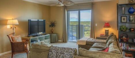 A living room with a television, two sofas, a chair, a bookshelf, and a balcony with a view.