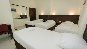 A hotel room with three single beds, a desk, a chair, and a large mirror.