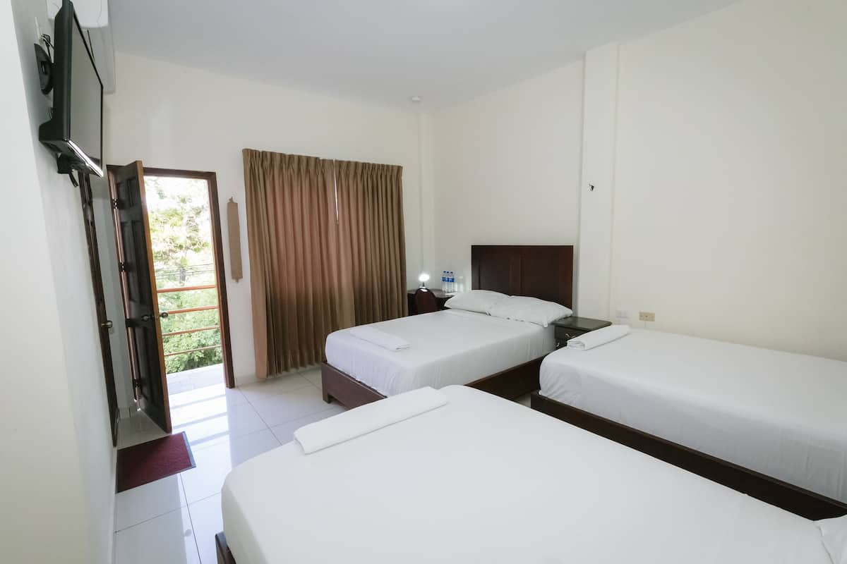 Quarto de hotel com duas camas de solteiro, uma televisão, uma mesinha de cabeceira e uma janela com cortinas.