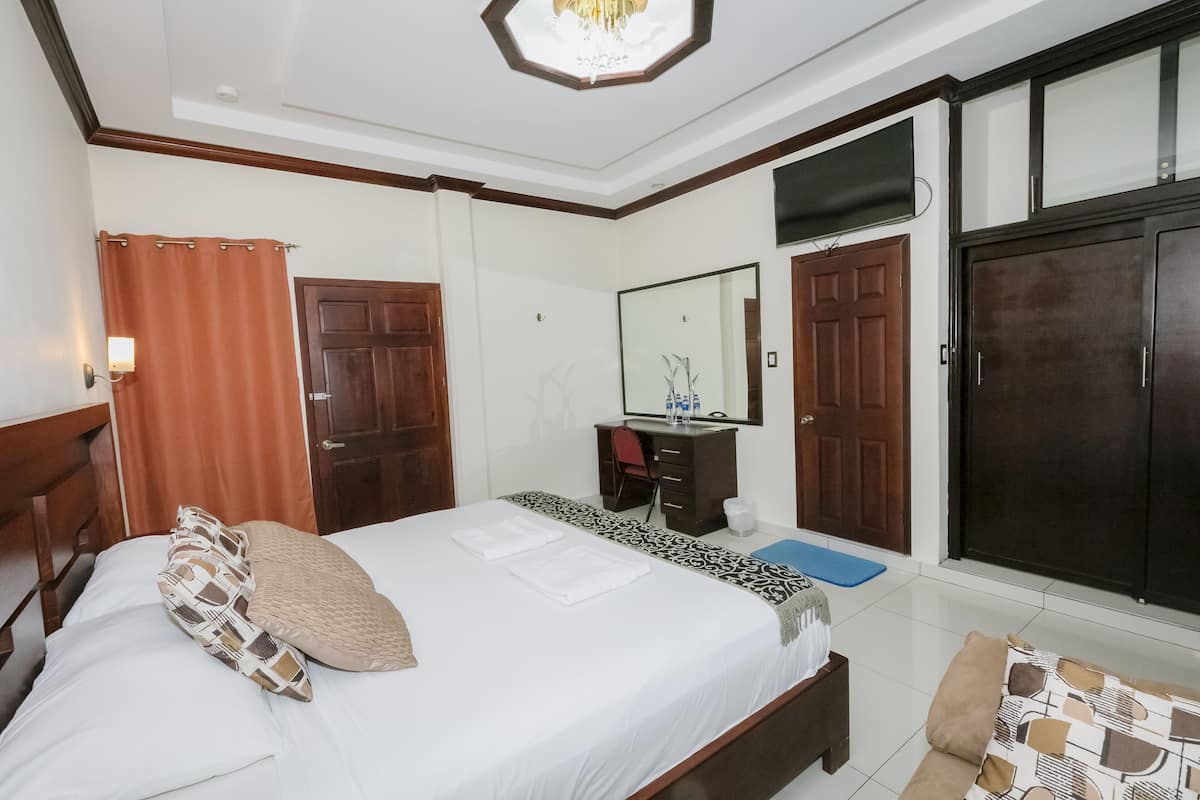Quarto de hotel com cama, escrivaninha, espelho e armários.