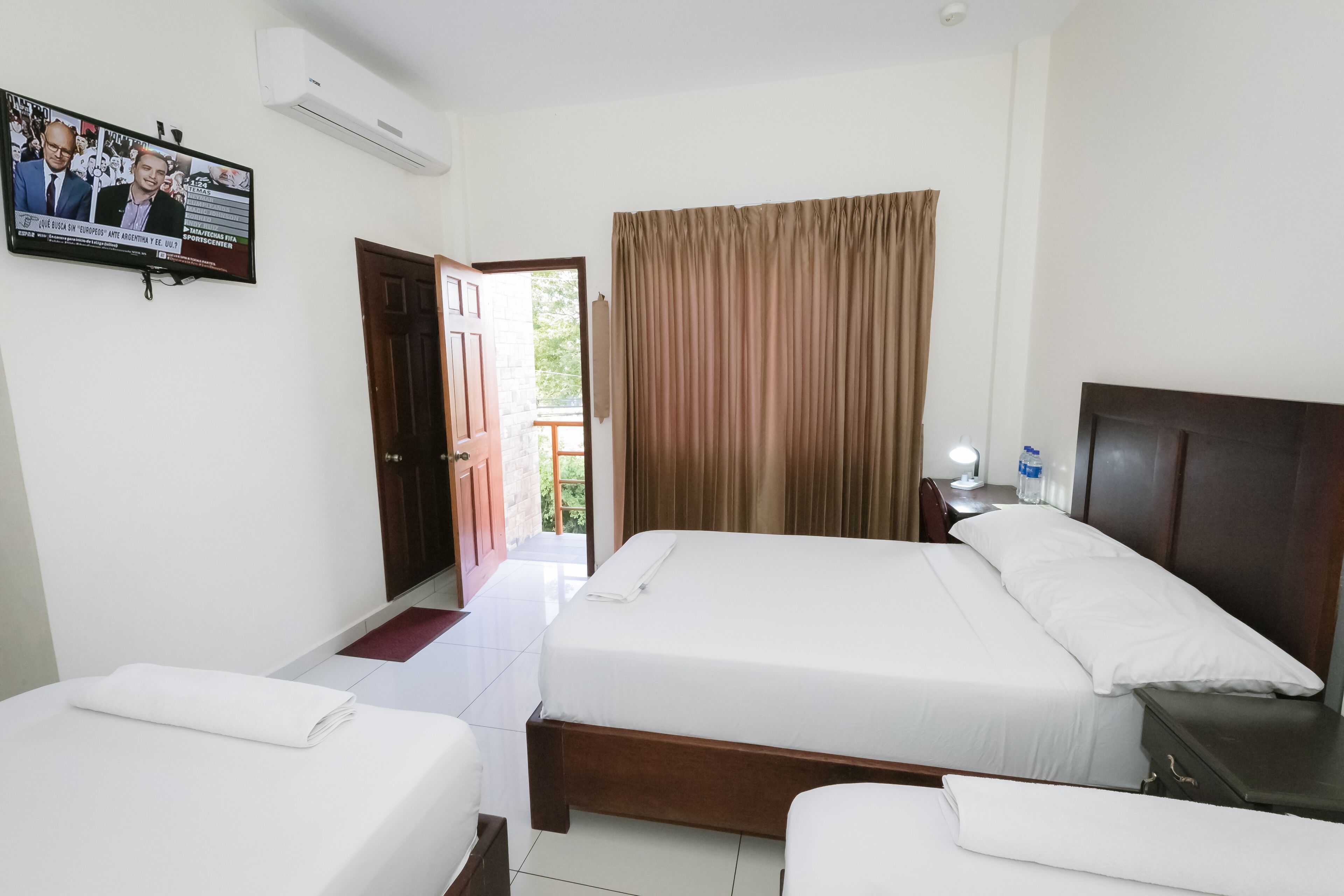 A hotel room with two beds, a TV mounted on the wall, and a window with curtains.
