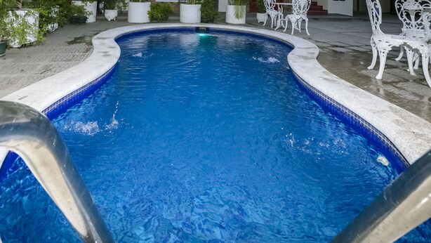 A swimming pool with a tiled edge, surrounded by potted plants and white outdoor furniture.