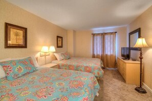 A hotel room with two beds, a TV on a wooden dresser, and a lamp.