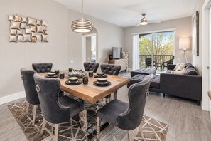 A modern dining area with a wooden table and upholstered chairs, a ceiling fan, and a balcony with outdoor seating.