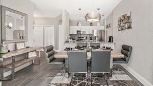 Een moderne keuken met een centraal eiland, roestvrijstalen apparatuur en een eethoek met een houten tafel en stoelen.