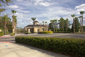 A building with a central dome and a tower, surrounded by palm trees and a well-maintained hedge.