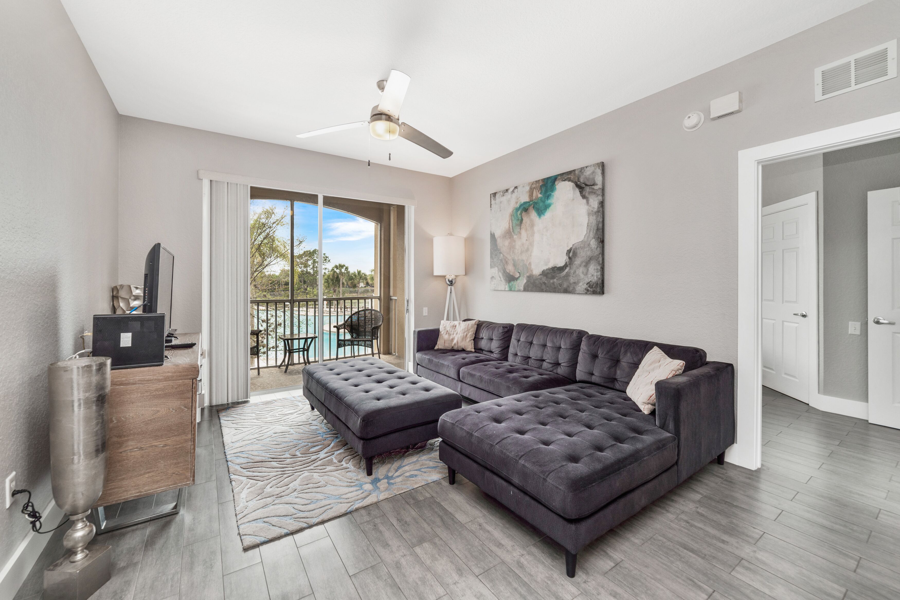 A modern living room with a sectional sofa, a flat-screen TV, and a ceiling fan.
