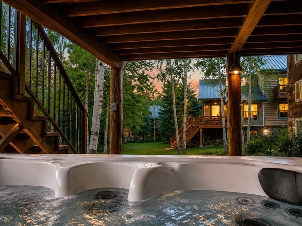 Un jacuzzi con terraza de madera y vista a una cabaña y árboles.