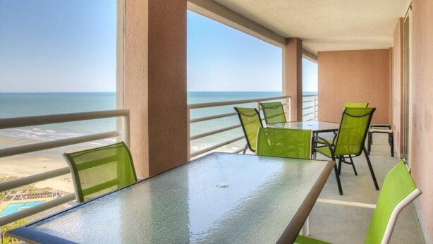 A balcony with a glass table and chairs, overlooking a beach and ocean. - Comfortable/spacious Villa at Kingston Plantation (Myrtle Beach)