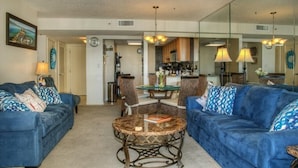 A living room with blue sofas, a round coffee table, and a dining area with a kitchen in the background. - Comfortable/spacious Villa at Kingston Plantation (Myrtle Beach)