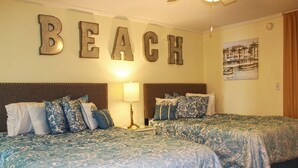A hotel room with two beds, a wall-mounted sign that reads "BEACH", a lamp, and a painting of a coastal scene. - Ocean Dunes Condo Rental - Right Near the Sands (Myrtle Beach)