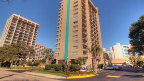 A high-rise building with multiple balconies, surrounded by greenery and parked cars. - Ocean Dunes Condo Rental - Right Near the Sands (Myrtle Beach)