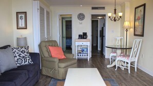 A living room with a sofa, armchair, coffee table, and dining area with chairs and a lamp. - Ocean Dunes Condo Rental - Right Near the Sands (Myrtle Beach)