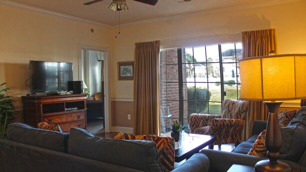 A living room with a sofa, a coffee table, a TV on a stand, and a view of the outdoors through a glass door. - Great Views of the Pool and Grilling Area! (Myrtle Beach)
