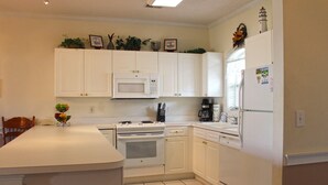 A kitchen with white cabinets, a microwave, stove, and refrigerator. There are plants on the upper cabinets and a fruit bowl on the counter. - Great Views of the Pool and Grilling Area! (Myrtle Beach)