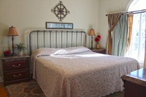 Un lit bien fait, recouvert d’une couvre-lit à motifs, deux tables de chevet avec des lampes, un élément décoratif mural et une fenêtre avec des rideaux.