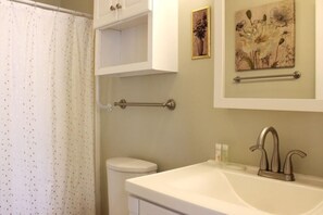 Une salle de bain comprenant des toilettes, un lavabo avec un robinet moderne, un porte-serviettes et un rideau de douche.