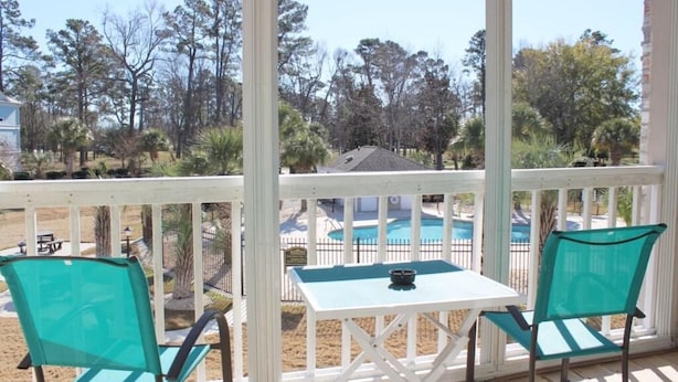 A covered outdoor seating area with two chairs and a table, overlooking a swimming pool and trees. - Peacefulmyrtlewood Villa Right in the Heart of MB (Myrtle Beach)