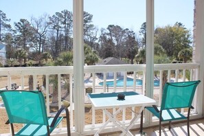 Un espace extérieur aménagé, abrité et doté de deux chaises et d’une table, offrant une vue sur une piscine et des arbres.