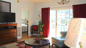 A living room with a television, a sofa, a coffee table, and a lamp. There is a window with curtains and a view of the outside. - Peacefulmyrtlewood Villa Right in the Heart of MB (Myrtle Beach)