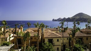 A coastal town with terracotta-roofed buildings, palm trees, and a view of the sea and a distant island. - Hacienda Beach Club Oceanview 4BR home– Prime Cabo Location (Cabo San Lucas,)