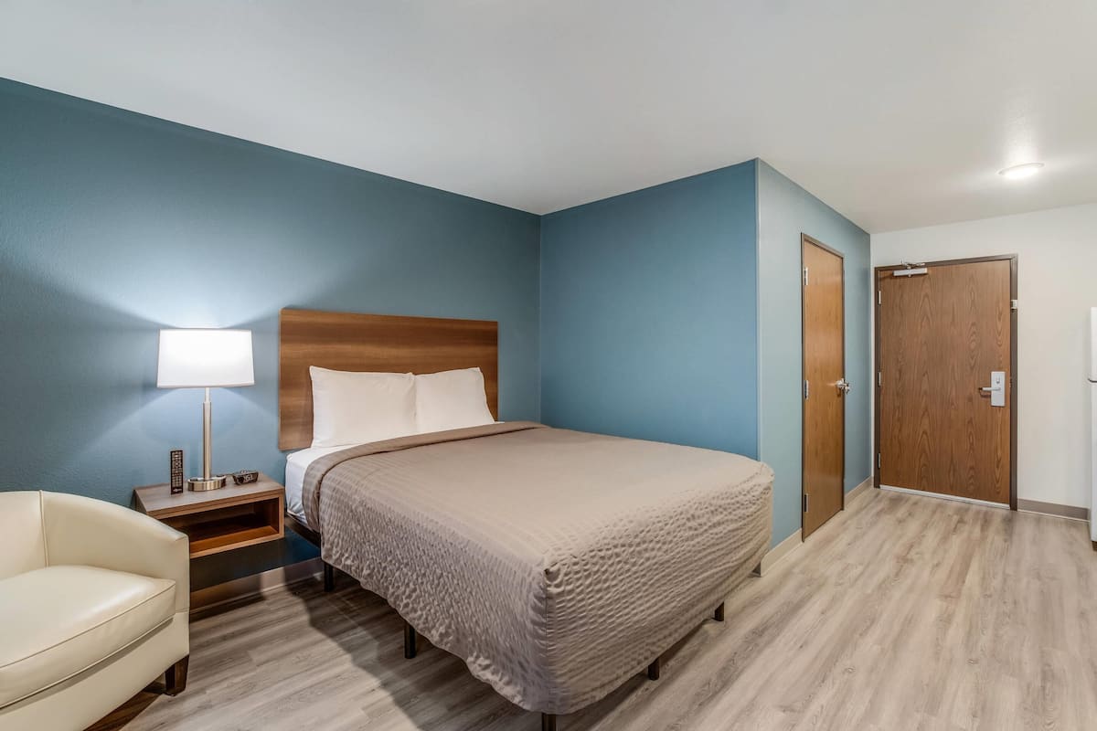 A hotel room with a bed, bedside table, lamp, and a chair.