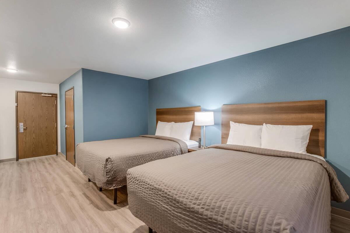 A hotel room with two beds, wooden headboards, a nightstand with a lamp, and a wooden door.