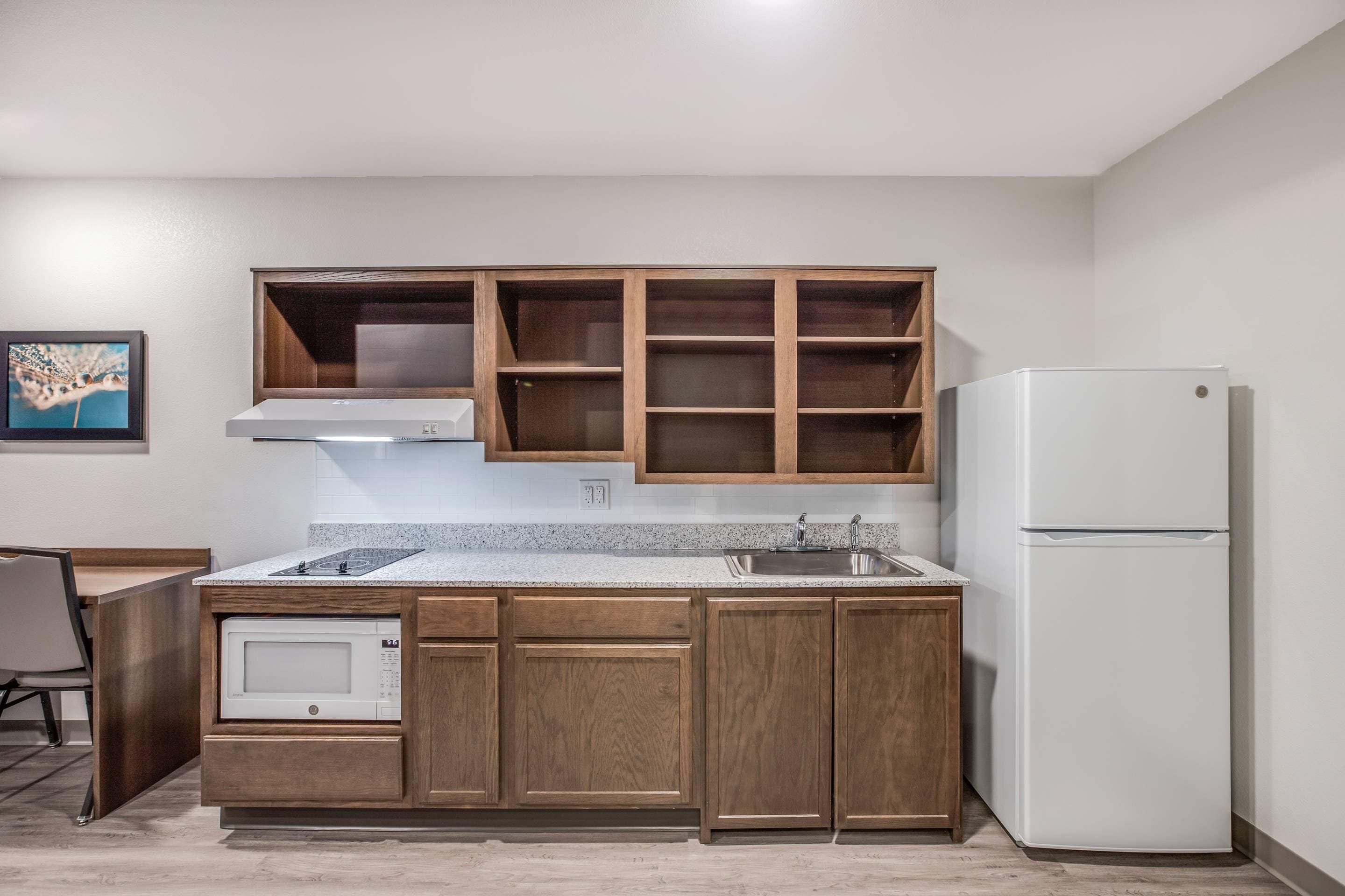 A compact kitchen with wooden cabinets, a built-in microwave, a sink, and a white refrigerator.