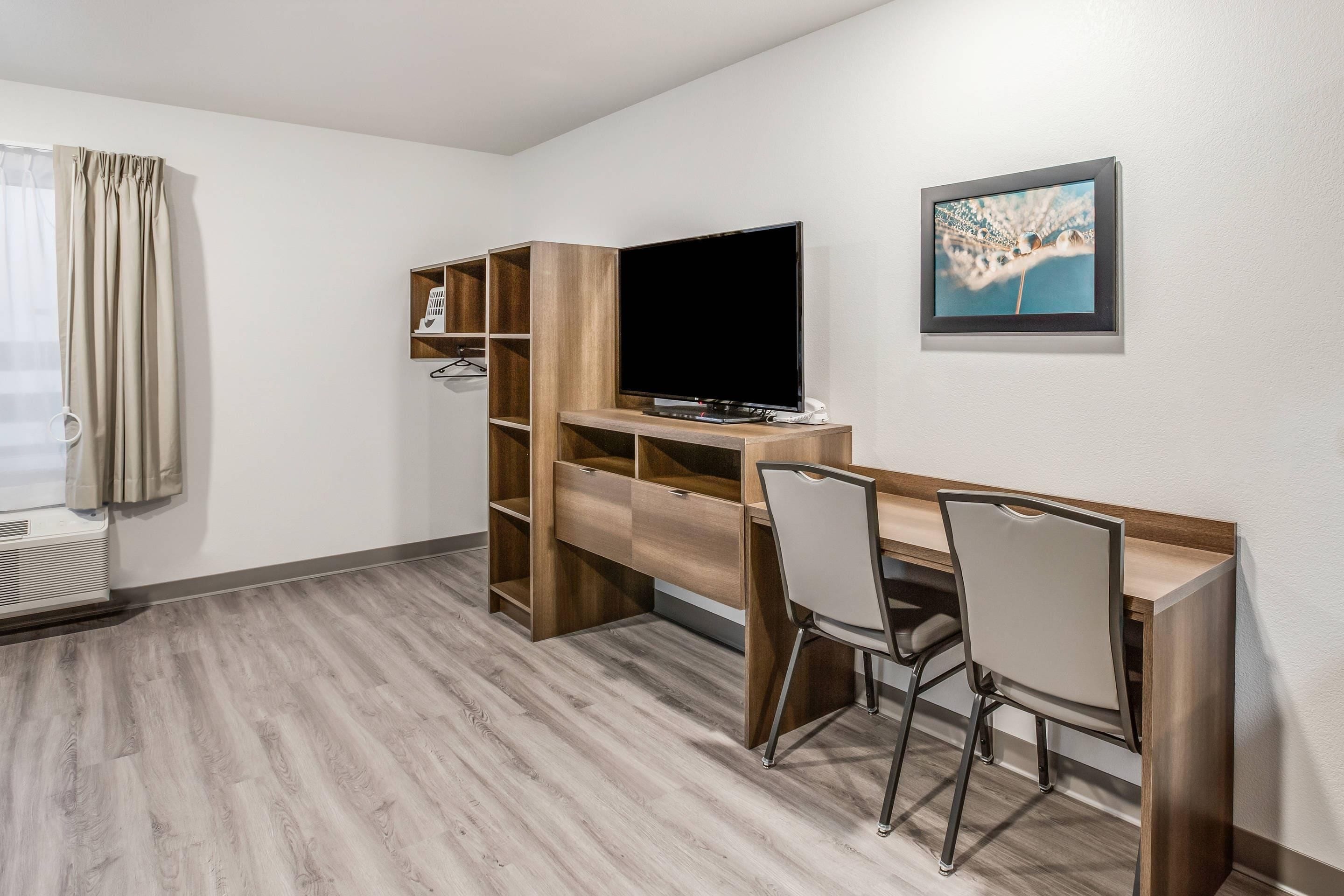 A hotel room with a wooden desk, a television, a chair, and a picture on the wall.