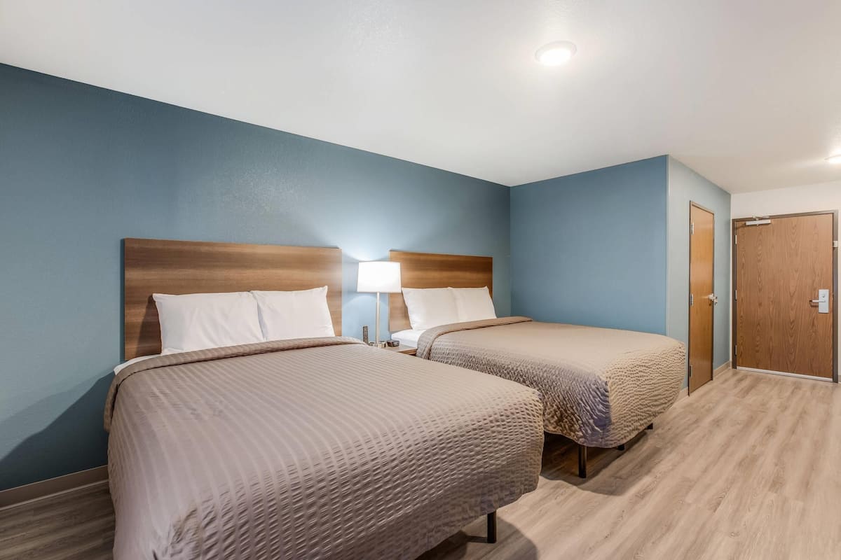 A hotel room with two beds, a wooden door, and a light blue wall.