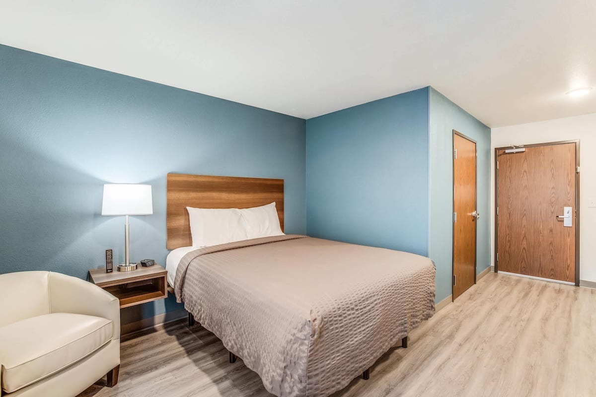 A hotel room with a bed, bedside table, lamp, and a wooden wardrobe.