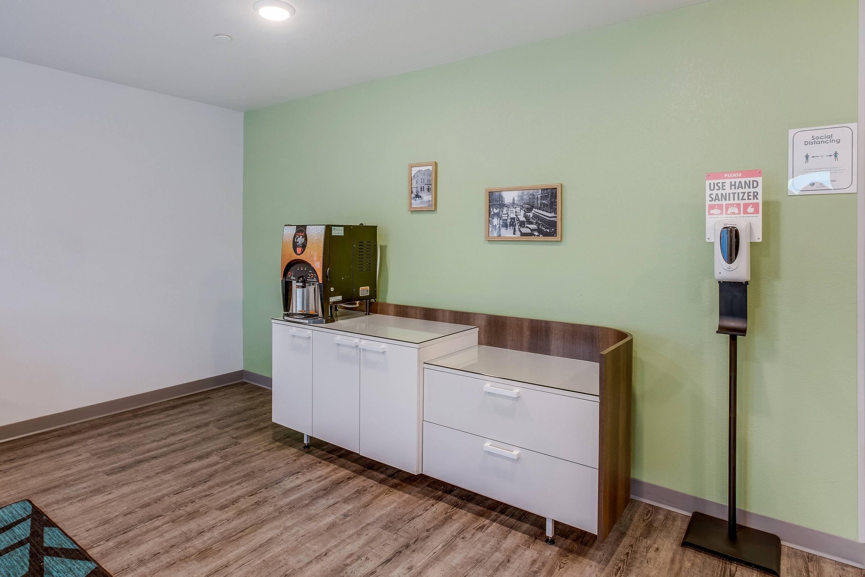 A reception area with a coffee machine, hand sanitizer dispenser, and a sign promoting social distancing.