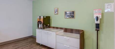 A reception area with a coffee machine, hand sanitizer dispenser, and a sign promoting social distancing.