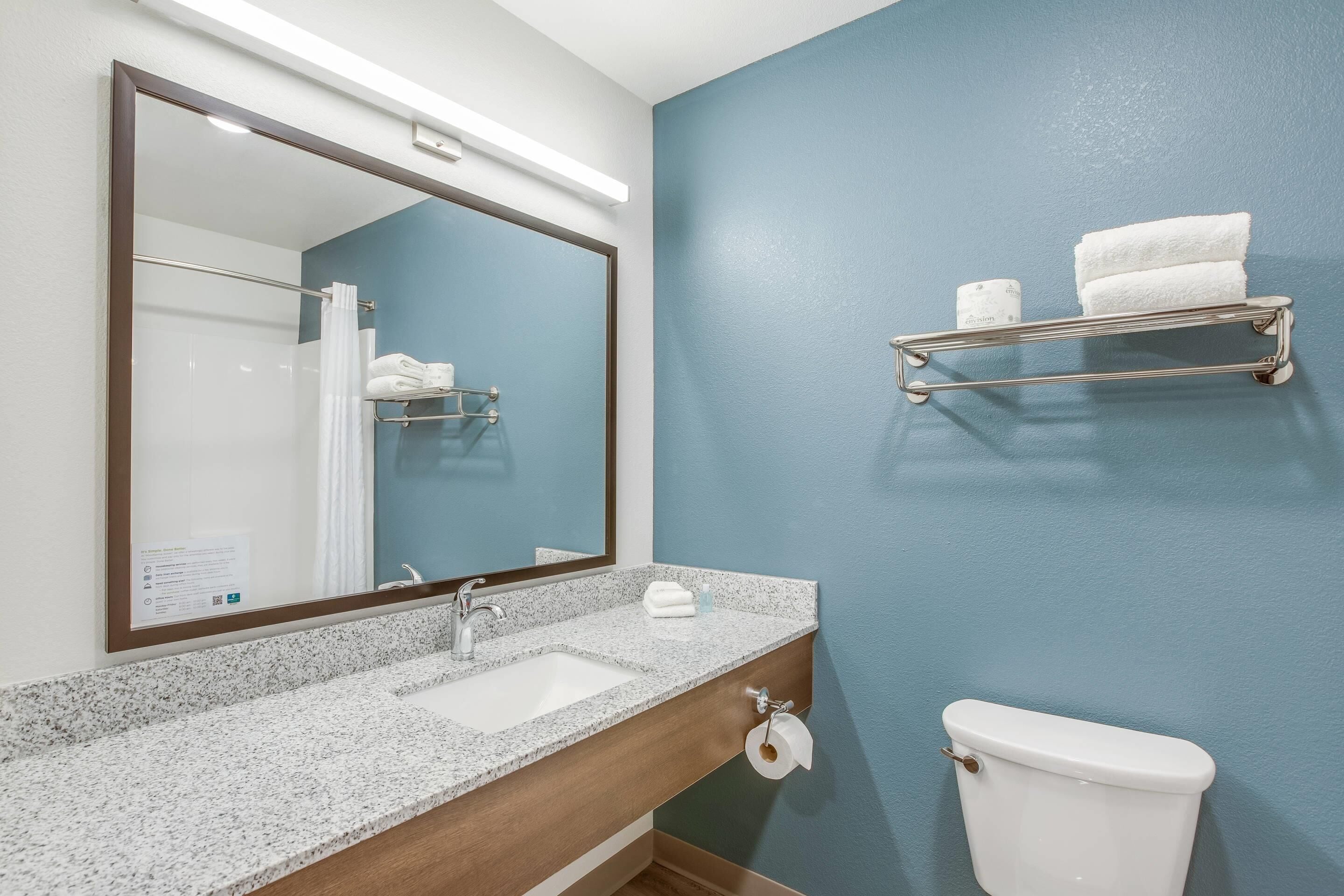 Un bany amb un lavabo de superfície de granit, un mirall, un penjallavops i un vàter.