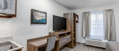 Moderni hotellihuone, jossa on puinen työpöytä, litteänäyttöinen televisio, sisäänrakennettu ilmastointilaite, sänky ja ikkuna, jossa on verhot.