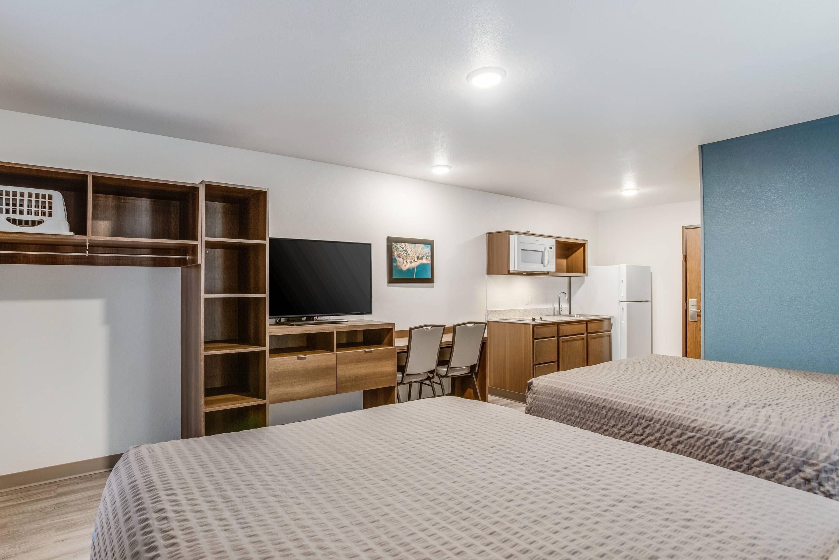 A hotel room with two beds, a desk with a chair, a television, a microwave, and a refrigerator.