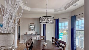 A dining area with a wooden table and chairs, a hanging light fixture, and a view of the outside through large windows. - Five Minute Walk to the Beach Sleeps 11 (Cape Charles)